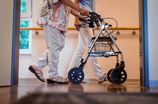 Eine Pflegekraft geht in einem Pflegeheim mit einer älteren Dame über einen Korridor.