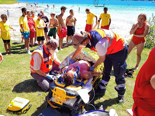Am Ufer des Strandbad Öhningen übernehmen die Sanitäter und Bereitschaftskräfte des DRK den verletzten Wassersportler. Sie überprüfen ...