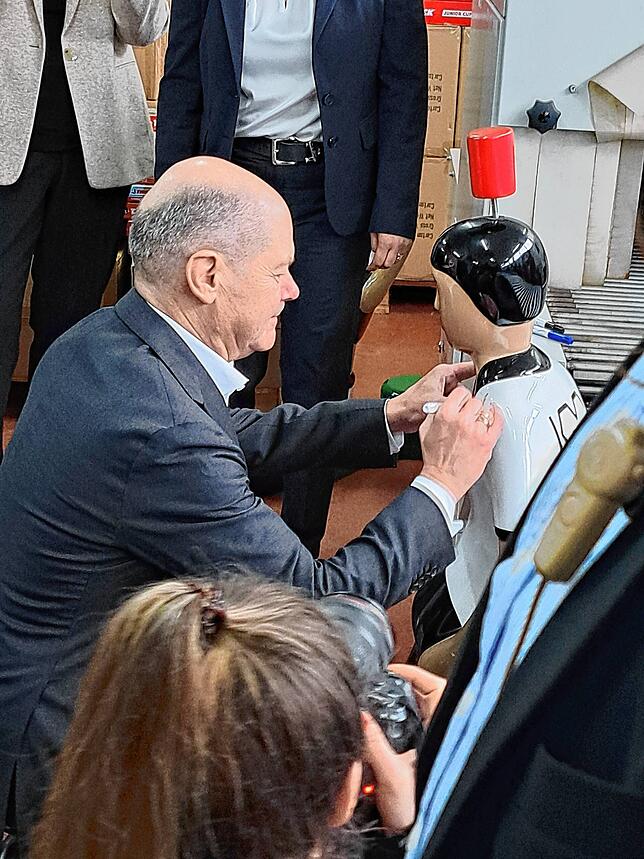 Olaf Scholz signiert eine große Tipp-Kick-Figur.