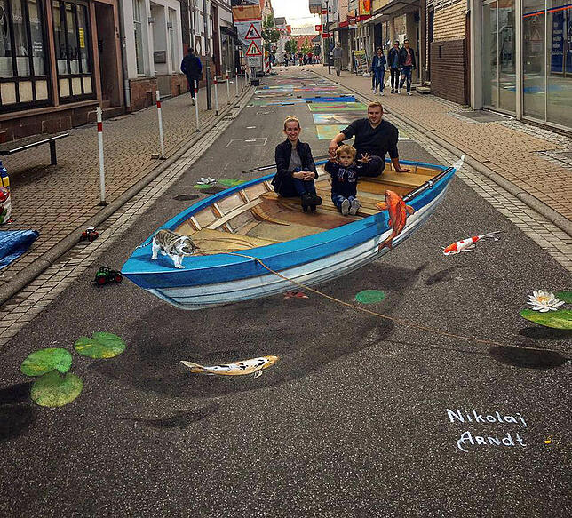 Das ist 3D-Kunst: Ein „Boot“ steht mitten auf der Straße und darin sitzt eine Familie.